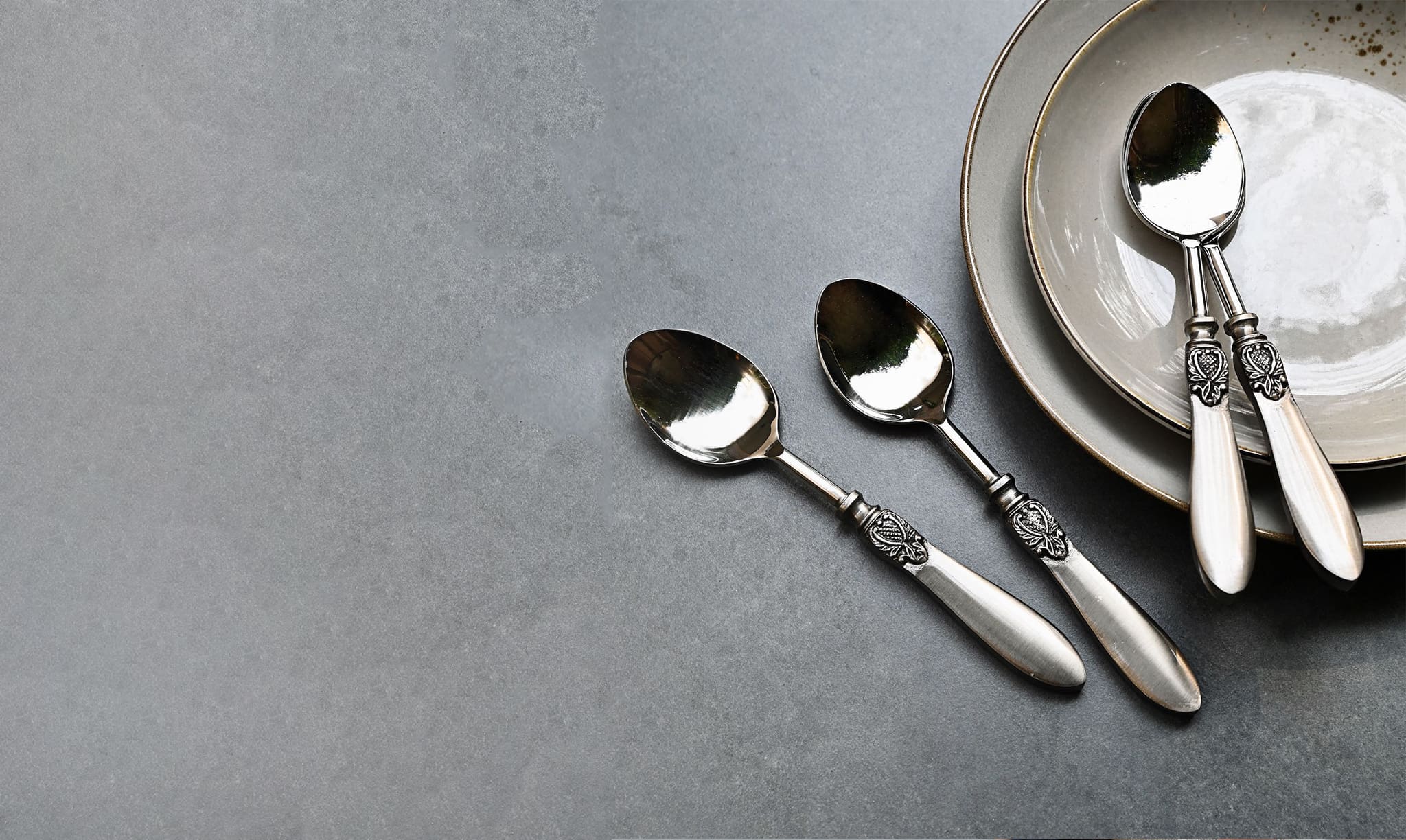 Silver spoons resting on a grey table beside an empty plate, evoking the spoon theory of limited capacity in relationships, by Victoria Onken